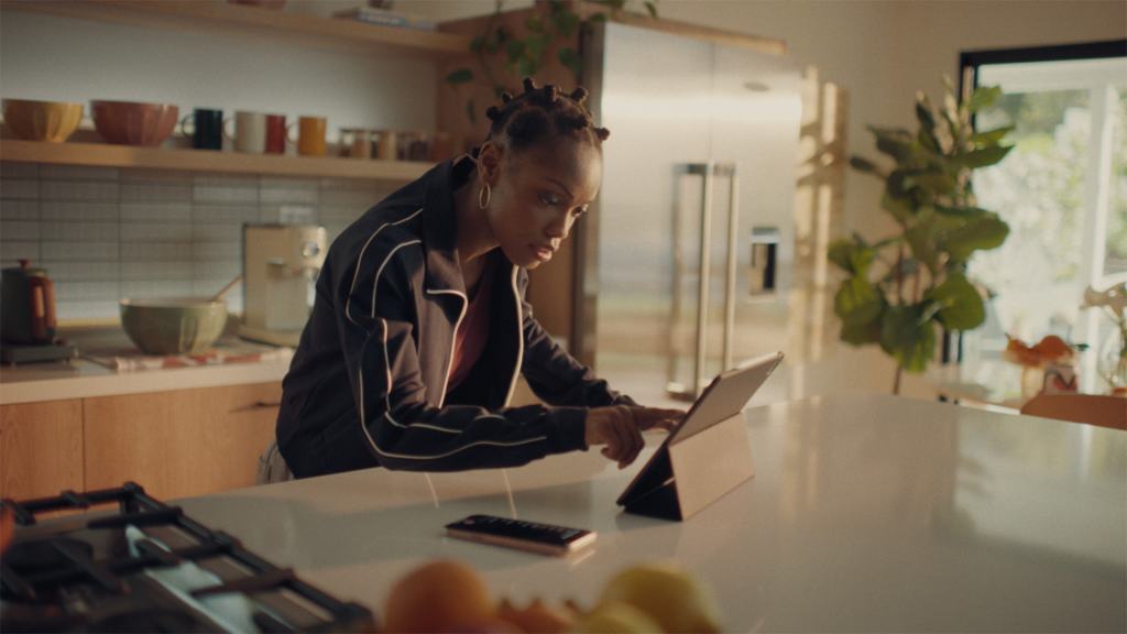 A person focused on using a tablet in a kitchen setting, surrounded by various kitchen items and plants.