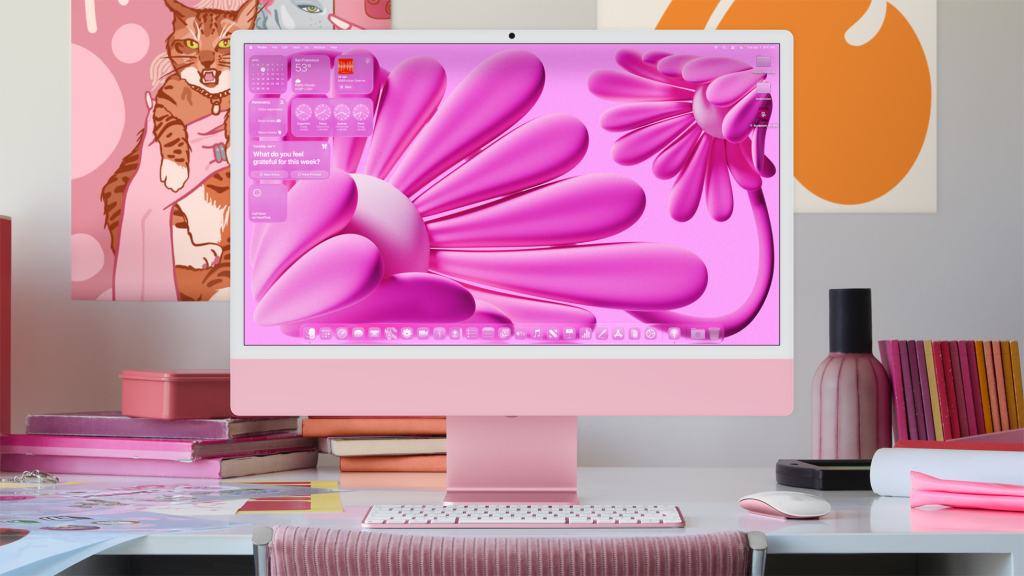 부드러운 핑크색의 디자인으로 꾸며진 Apple iMac이 책상 위에 놓여 있고, 화면에는 생동감 있는 꽃 패턴의 배경과 다양한 위젯이 표시되고 있다.