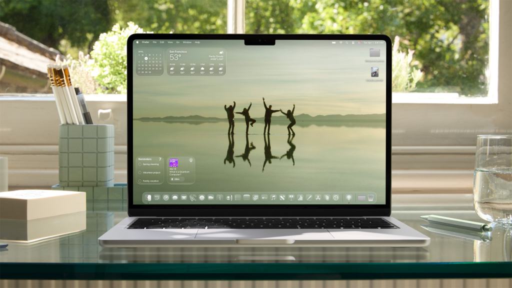 A Mac laptop displaying a serene desktop background showing silhouetted figures dancing on water, with the macOS Tahoe 26 interface visible.