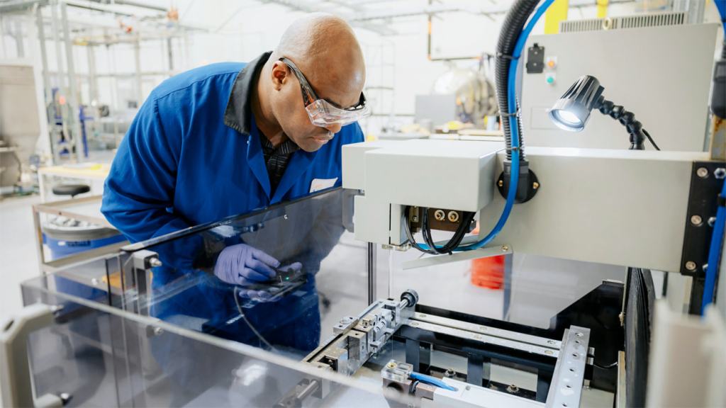 A technician wearing safety goggles examines machinery in a high-tech packaging facility.