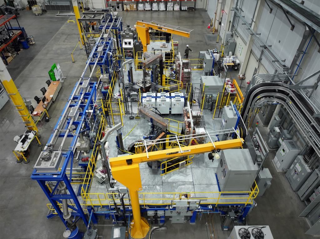 Aerial view of a modern manufacturing facility featuring advanced packaging machinery for semiconductor components, with yellow cranes and production equipment visible.