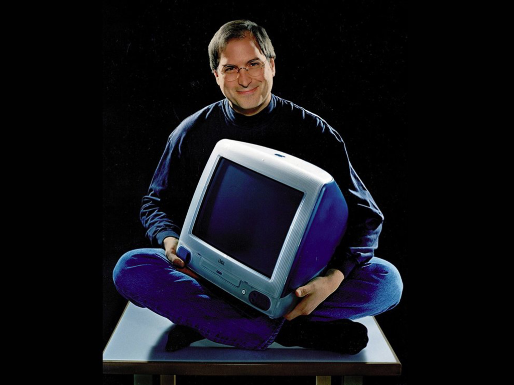 스티브 잡스가 매킨토시 컴퓨터를 끌어안고 앉아 있는 모습