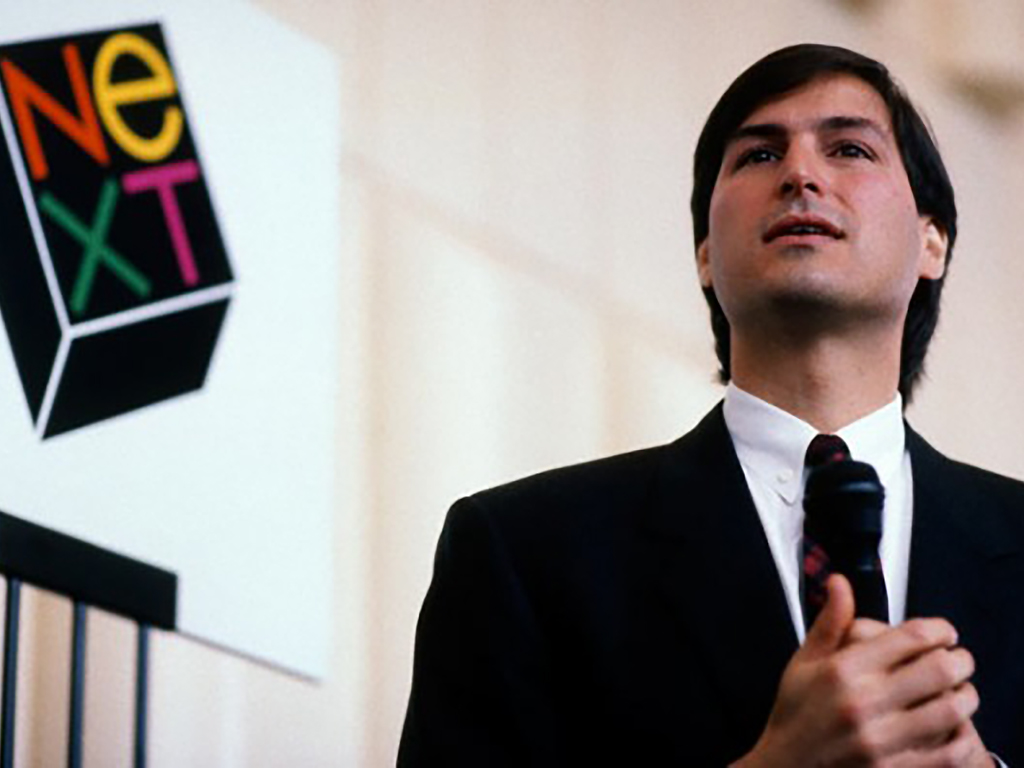 스티브 잡스가 NeXT 제품 발표 중 연설하고 있는 모습. 배경에는 NeXT 로고가 보인다.