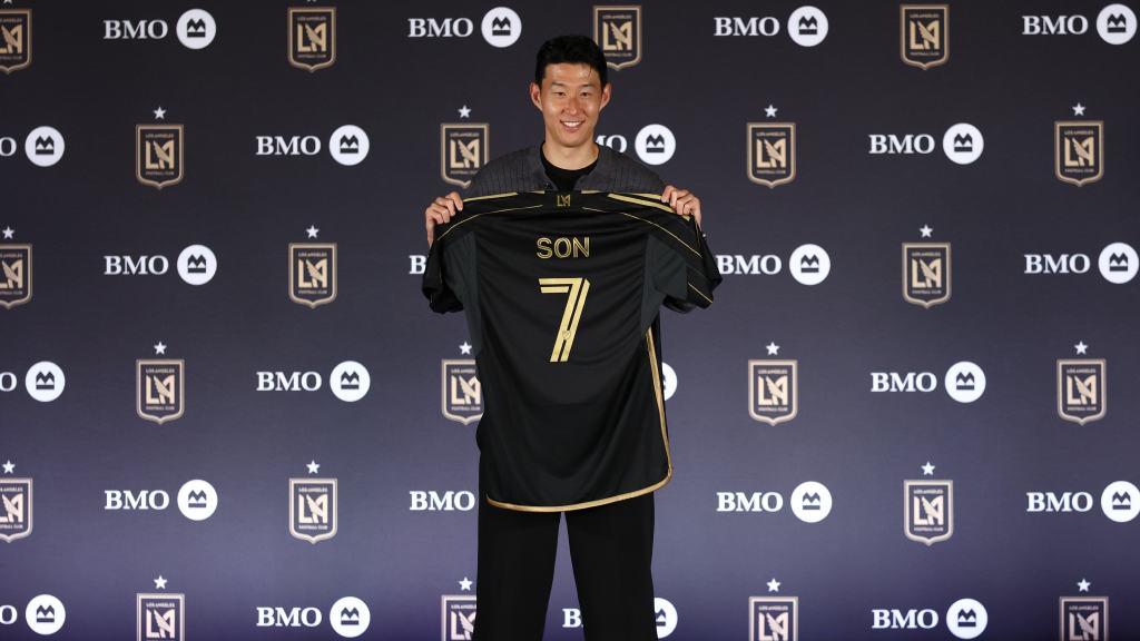 손흥민이 LAFC 유니폼을 들고 포즈를 취하고 있는 모습, 배경에는 LAFC 로고가 있는 기자회견 장면