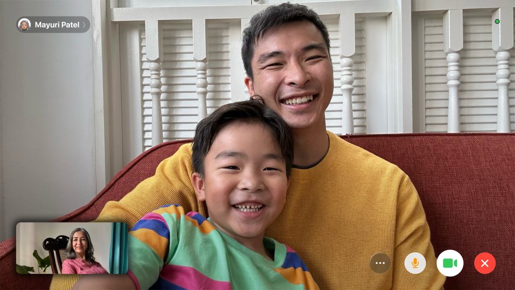 A happy young boy and a man smiling together while participating in a video call, with a woman visible in a smaller window on the screen.