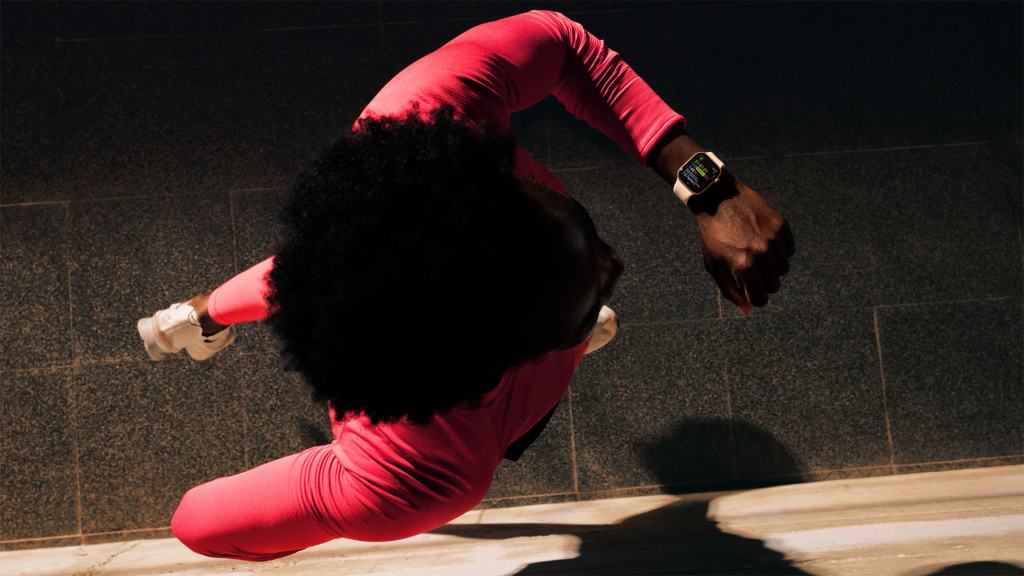 A person wearing a pink athletic outfit is running while checking their smartwatch.