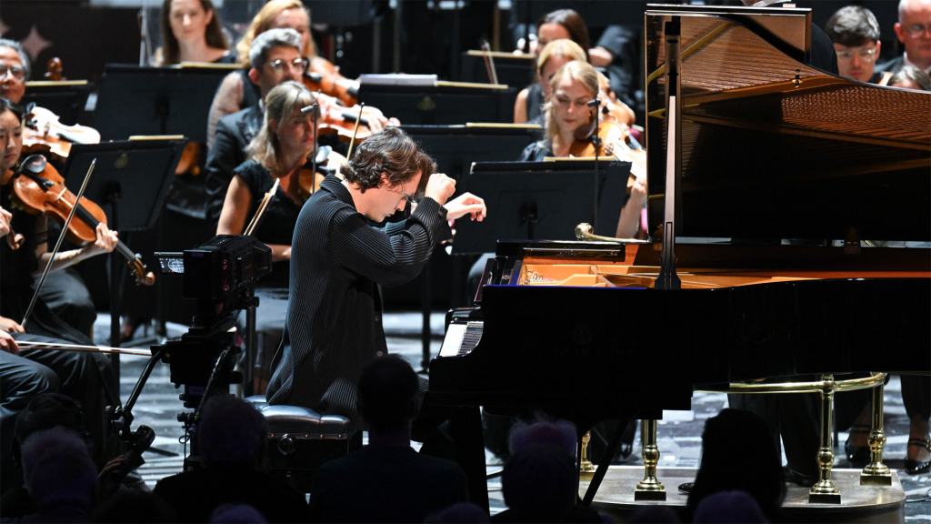 A pianist performing at a classical music concert with an orchestra in the background, showcasing a captivating immersive experience.