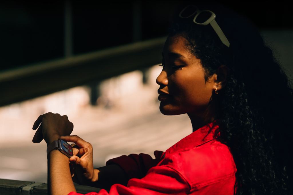 A woman in a red jacket is checking her Apple Watch outdoors, with a focus on her wrist and the watch face.